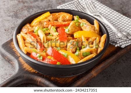 Rasta Pasta is a Penne cooked in rich creamy sauce with Jerk Chicken, sauteed onions, Sweet Peppers, garlic closeup on the bowl on the wooden board. Horizontal
