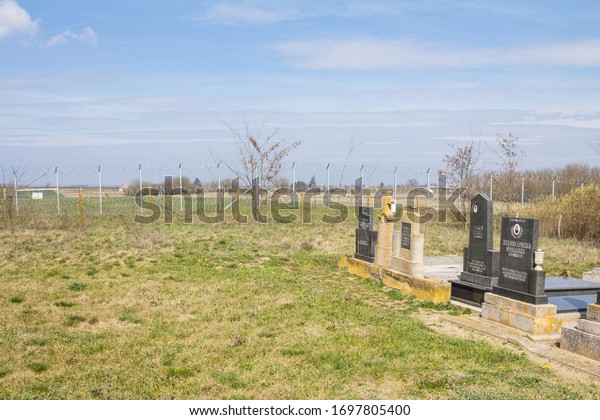 RASTINA, SERBIA - MARCH 19, 2016: Serbian\
Orthodox Cemetary of Rastina cut by the Border fence between Serbia\
& Hungary, built in 2015 to stop the incoming refugees during\
the refugees\
crisis.\
\

