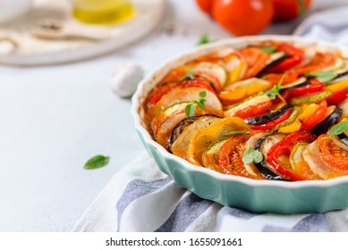 Ratatouille Casserole On White Background. Colorful Layers Of Fresh Summer Vegetables: Zucchini, Eggplant, Tomatoes And Potatoes. Healthy Vegan, Vegetarian Dish. Side View, Copy Space. Menu, Recipe