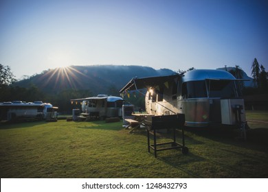 Ratchaburi / Thailand - Jan 22, 2018: Caravan camping campsite of American Airstream travel trailers parking in the yard in the sunrise morning with mountain and fog in the background.