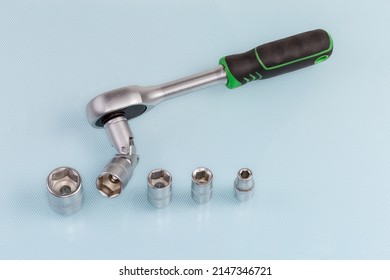 Ratchet wrench with hexagonal socket which was inserted via a gimbal joint adapter and the same several interchangeable sockets different sizes on a blue surface 