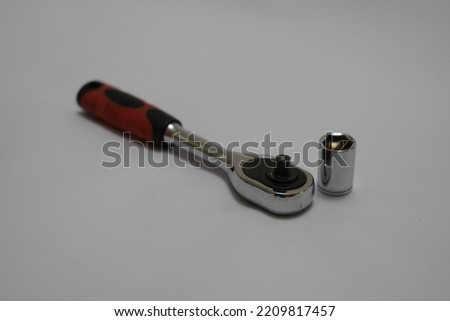  Ratchet wrench with rubberized handle with hexagonal socket which inserted via a gimbal joint adapter lies on a light surface 