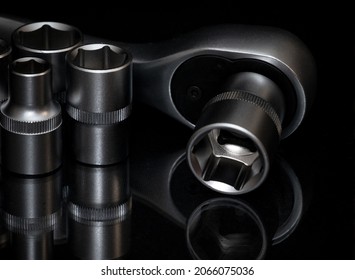 Ratchet wrench. Set of stainless steel hex sockets on shiny black surface. Universal professional tool for car repair. Low key photo.