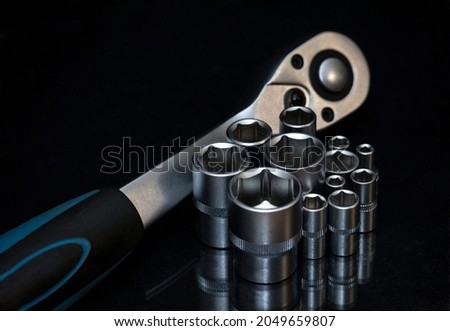 Ratchet wrench. Set of stainless steel hex sockets on shiny black surface. Universal professional tool for car repair. Low key photo.