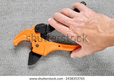 Ratcheting PVC pipe cutter, tube cutting tool for one-handed use, on gray background.