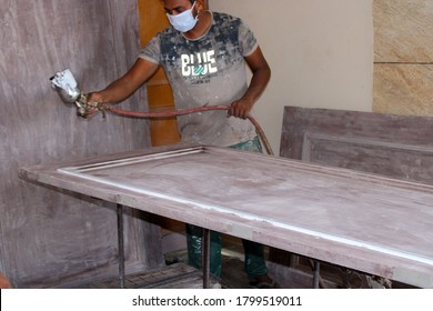Ratia, Haryana, India - 7 Aug, 2020: Painter Holding A Spray Gun And Painting Wooden Door In Home. Painting Cabinets With Spray Gun. Painting Chamber, Spray Gun. Wooden Furniture Manufacturing Process