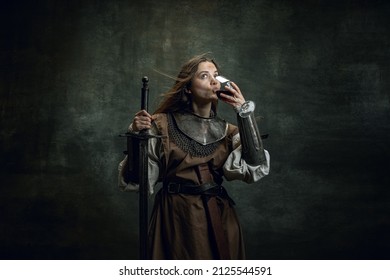 Rating Red Wine. Vintage Portrait Of Adorable Woman, Medieval Female Warrior Or Knight With Dirty Wounded Face With Sword Isolated Over Dark Background. Comparison Of Eras, History, Renaissance Style