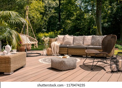 A rattan patio set including a sofa, a table and a chair on a wooden deck in the sunny garden. - Powered by Shutterstock