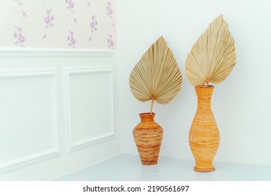 Rattan Pots With Dried Palm Leaves Are Placed Next To A Floral Patterned Wall And Molding Isolated On White Background. Photo Studio Property Decoration. Interior Design.