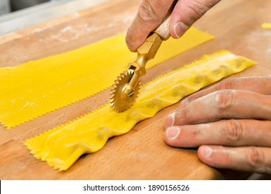 Ravioli del plin, typical pasta of Langhe, Piedmont, Italy - hand cutting with rotary knife of agnolotti on wooden cutting board