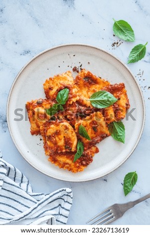 Ravioli with ricotta, tomato sauce and basil, white marble background, top view.