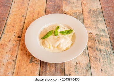 Ravioli Stuffed With Cheese Covered With Béchamel Sauce And Basil Leaves On Wooden Table