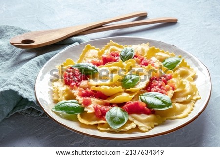 Ravioli with tomato sauce and fresh basil leaves, Italian recipe, on a slate background with a wooden spoon