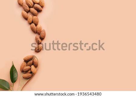 Raw almond kernels in wooden spoon on beige background, green herbs. Cosmetic and healthy food concept, Isolated and flat lay. High quality photo