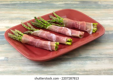 Raw Asparagus Bunches Wrapped In Prosciutto Slice N Red Plate In Preparation For Cooking