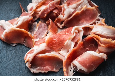 Raw bacon cut into thin slices on a black mica board. High quality photo