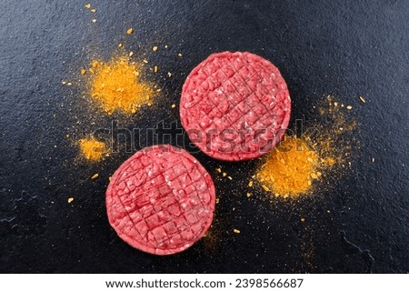 Raw barbecue beef Hamburger patty with exotically spice offered as top view on a rustic black board with copy 