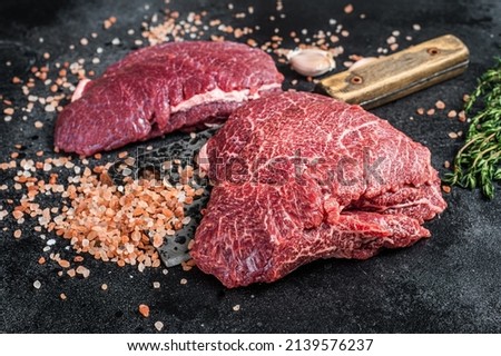 Raw Beef cheeks, fresh veal meat on butcher cleaver. Black background. Top view.
