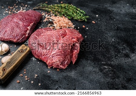 Raw Beef cheeks, fresh veal meat on butcher cleaver. Black background. Top view. Copy space.
