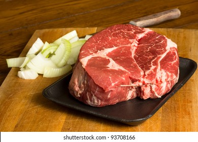 Raw Beef Chuck Roast On A Cutting Board With Chopped Onion In Preparation Of A Meal