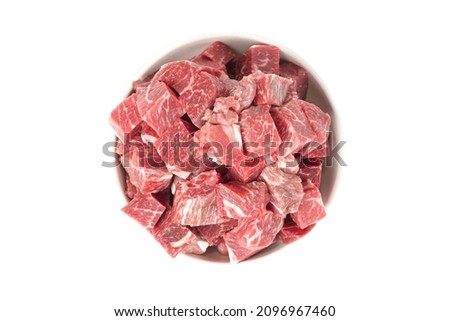 Raw beef cubes in a white ceramic bowl, fresh, natural dog or cat food, isolated on a white background.