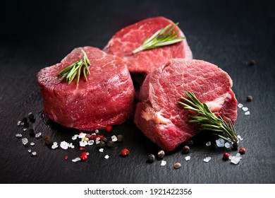 Raw beef filet mignon steaks with rosemary, pepper and salt on dark rustic board, black angus meat