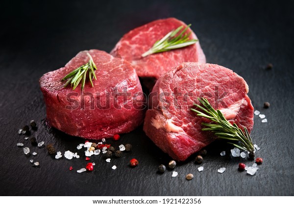 Raw beef filet mignon\
steaks with rosemary, pepper and salt on dark rustic board, black\
angus meat