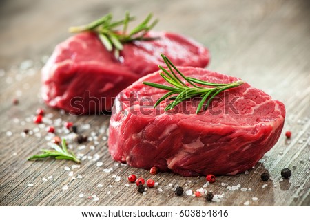 Raw beef fillet steaks with herbs and spices on wooden background