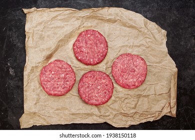 Raw Beef Hamburger Patties On Paper And Black Background, Overhead View. Raw Burger Cutlets On Isolated Background, Top View. Many Raw Minced Steak Burgers From Beef Pork Meat On Black Background.