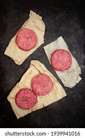 Raw Beef Hamburger Patties On Paper And Black Background, Overhead View. Raw Burger Cutlets On Isolated Background, Top View. Many Raw Minced Steak Burgers From Beef Pork Meat On Black Background.