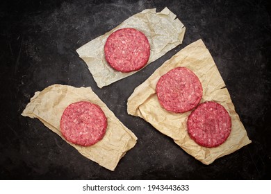 Raw Beef Hamburger Patties On Paper And Black Background, Overhead View. Raw Burger Cutlets On Isolated Background, Top View. Many Raw Minced Steak Burgers From Beef Pork Meat On Black Background.