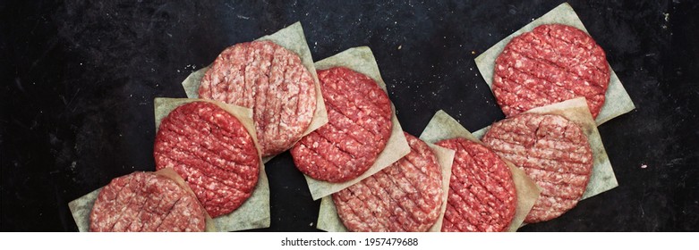 Raw Beef Hamburger Patties On Paper And Black Background, Overhead View. Raw Burger Cutlets On Isolated Background, Top View. Many Raw Minced Steak Burgers From Beef Pork Meat On Black Background.