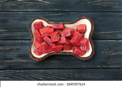 Raw Beef Meat In Bowl. Natural Food For Dog On Black Wooden Background. Top View.