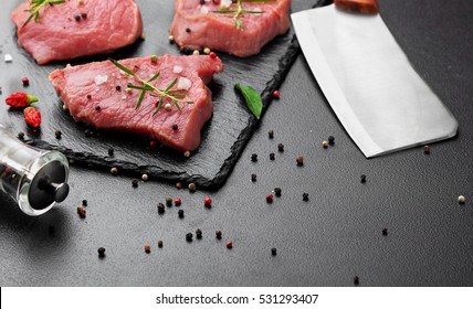 Raw beef meat with butcher knife on slate plate.Scattered black pepper, chili .Dark bakcground.Selective focus . copy space