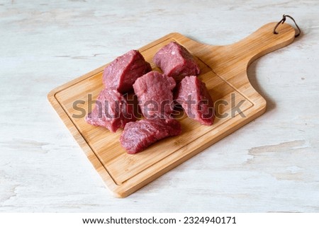 Raw beef meat on wooden cutting board for cooking stew or other meat dish on white background top view