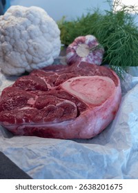 Raw beef shank with bone placed on parchment paper, surrounded by fresh cauliflower, garlic, and dill. Natural lighting and clean layout. Ideal for commercial use in food packaging, 
