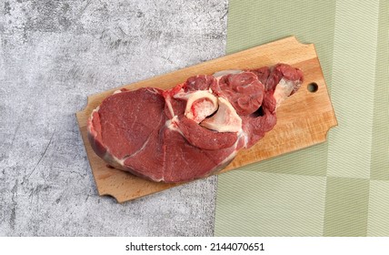 Raw beef shank on a rectangular cutting wooden board on a dark grey background. Top view, flat lay