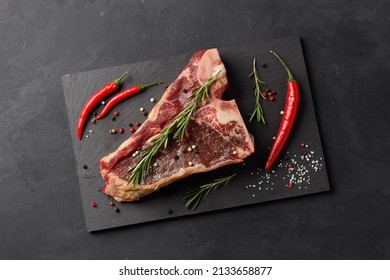 Raw Beef Steak, Dry Aged T Bone With Red Hot Pepper And Spices On Black Cutting Board Background, Top View.