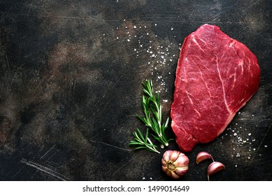 Raw beef steak with spices on a dark slate, stone or concrete background. Top view with copy space.