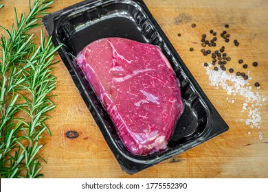 Raw beef steak in vacuum skin packaging and spices on wooden chopping board