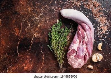 Raw beef tongue on kitchen table with herbs. Dark background. Top view. Copy space