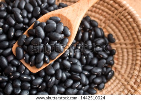 Raw black beans in basket and spoon on wood table. Black beans has health benefits they are source of protein, filling fiber, disease fighting antioxidants, and numerous vitamins and minerals.