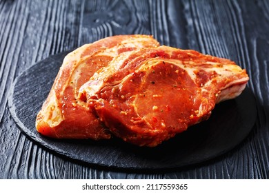 raw bone-in marinated pork chops on a black stone plate on a wood table, horizontal view - Powered by Shutterstock