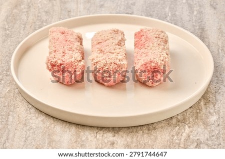 Raw breaded meat cutlets in breadcrumbs on plate. top view of raw breaded cutlets (minced meat patties) coated with golden breadcrumbs. The uncooked meat is partially visible through the breading.  Natural lighting, food preparation concept. Ideal for cooking blogs, recipe illustrations, frying instructions, or packaging design.