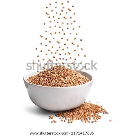 Raw buckwheat grains falling in bowl on white background