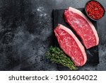 Raw cap rump steak or top sirloin beef meat steak on marble board. Black background. Top view. Copy space.