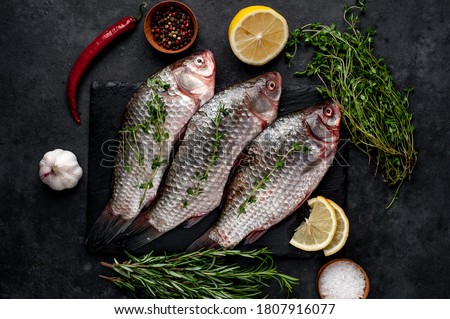 Raw carp with lemon and rosemary on a black plate on a stone background River organic fish