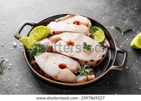 Raw catfish steaks with herbs, lime and spices in a baking dish on a gray background. High quality photo