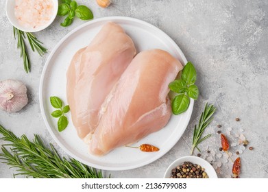 Raw chicken breast or fillet with salt, pepper and fresh herbs on a white plate on a gray background. Healthy food. Top view, copy space