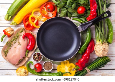 Raw chicken breast fillets with vegetables ingredients in wooden plate around frying pan for tasty diet. Top view. Food cooking background.